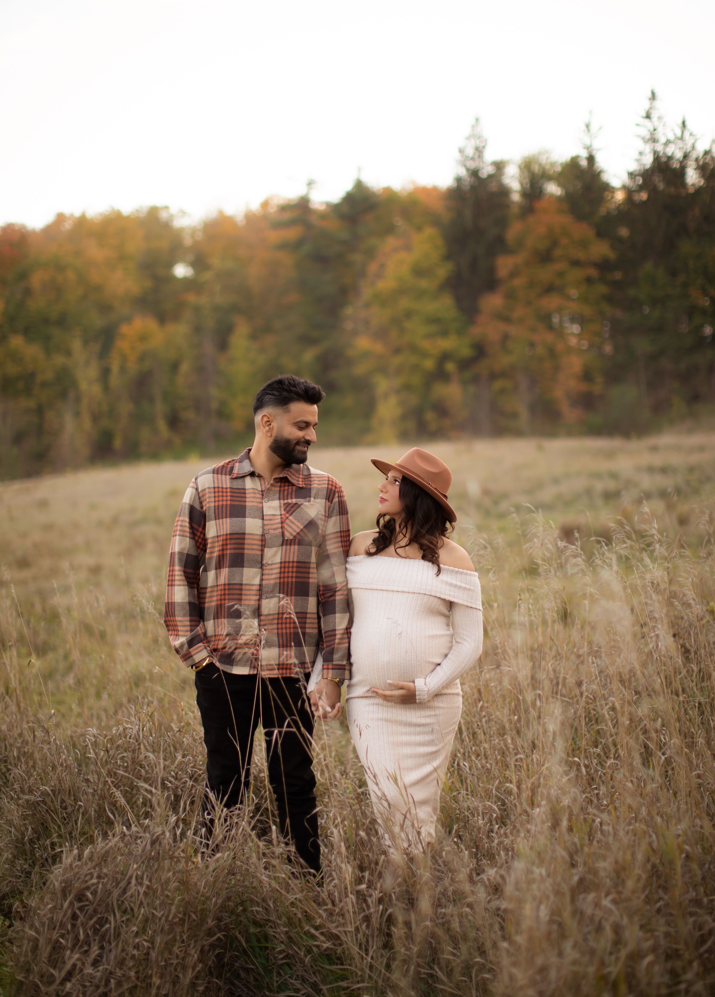 Couple embracing in autumn field during sunset maternity photoshoot.