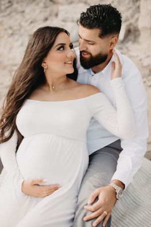 Intimate maternity couple photos on beach with white clothing and soft lighting.