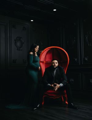 Moody maternity portraits in dark room with red accent chair creating dramatic atmosphere.