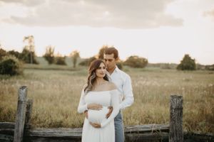 Romantic maternity photoshoot in a field with couple in white outfits at golden hour.