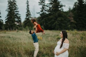 Couple playfully dancing together in grassy field with evergreen trees.