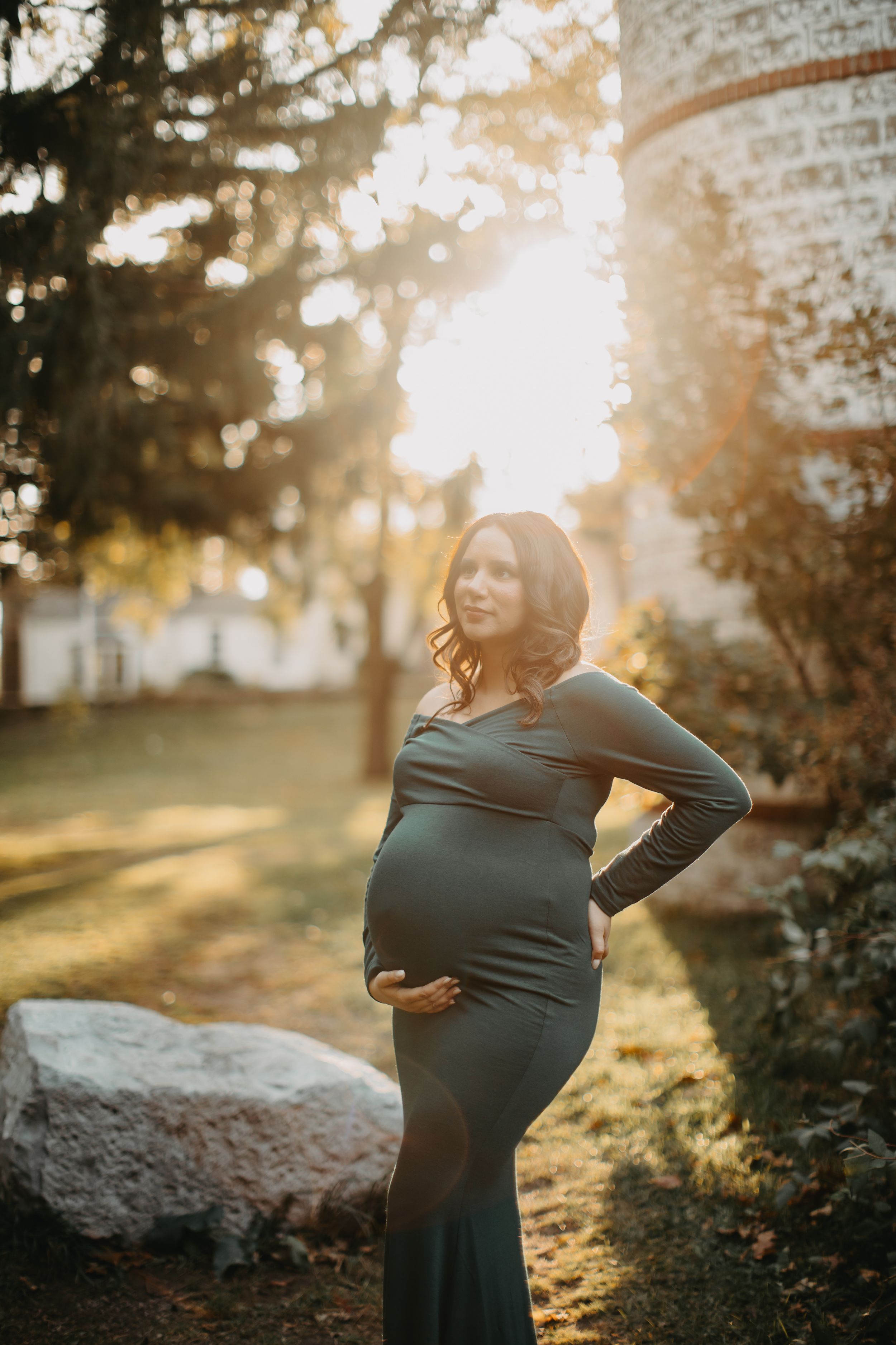 Silhouette of pregnant woman in green dress during golden hour outdoor photoshoot.