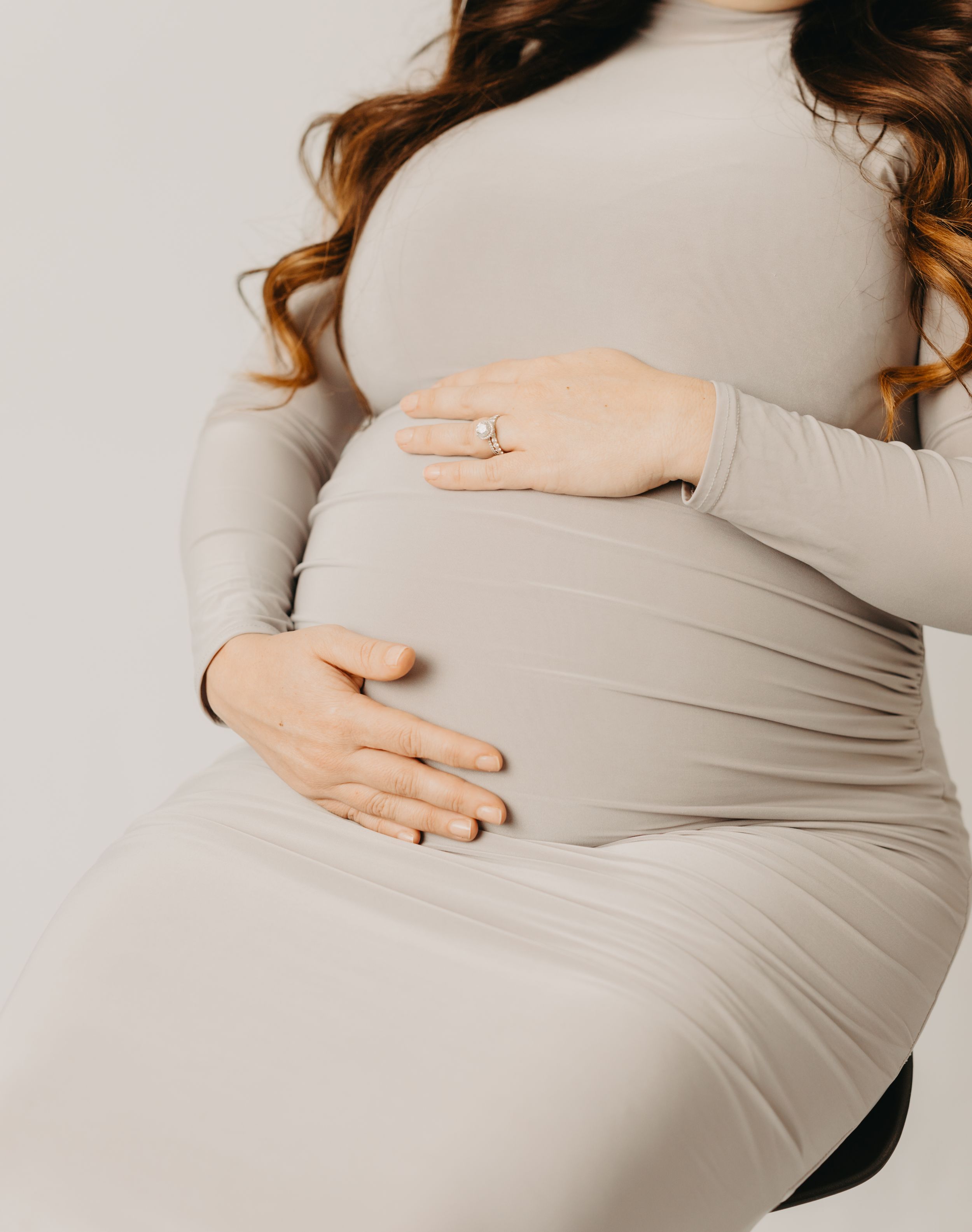 Close-up of hands cradling a pregnant belly in soft beige fabric.