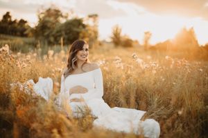 Dreamy maternity photos captured in field during golden hour with flowing white dress.