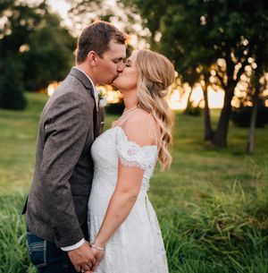 An intimate wedding kiss photographed in a sun-dappled garden setting.