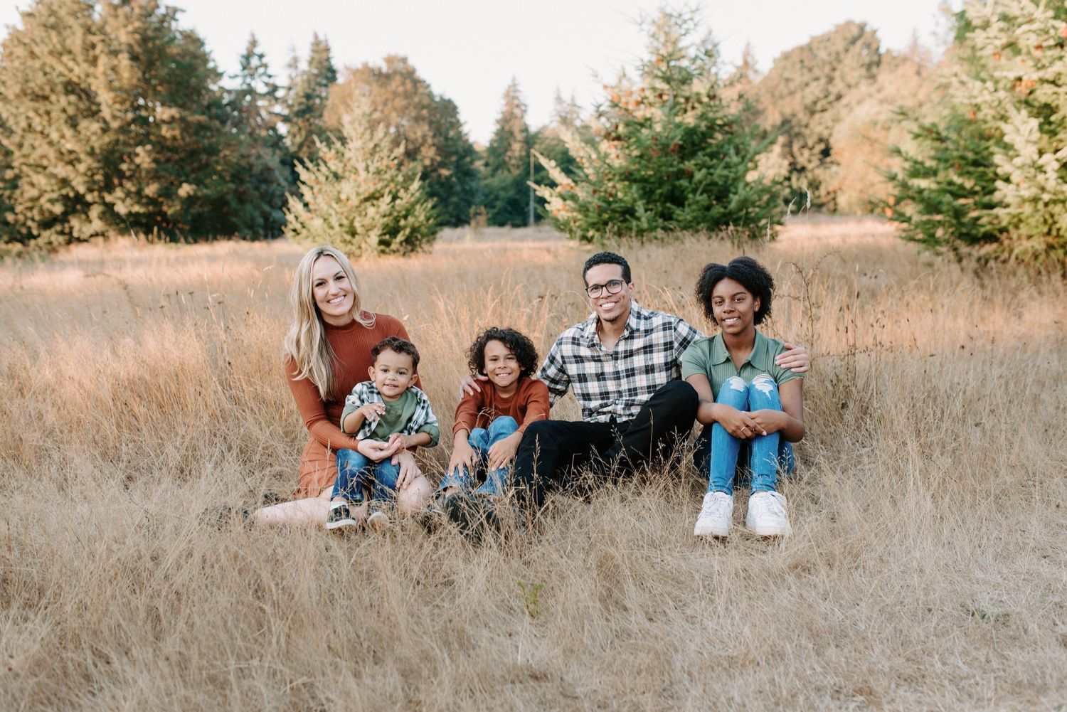 Family portrait session in a golden grass field with mountains and trees in the background.