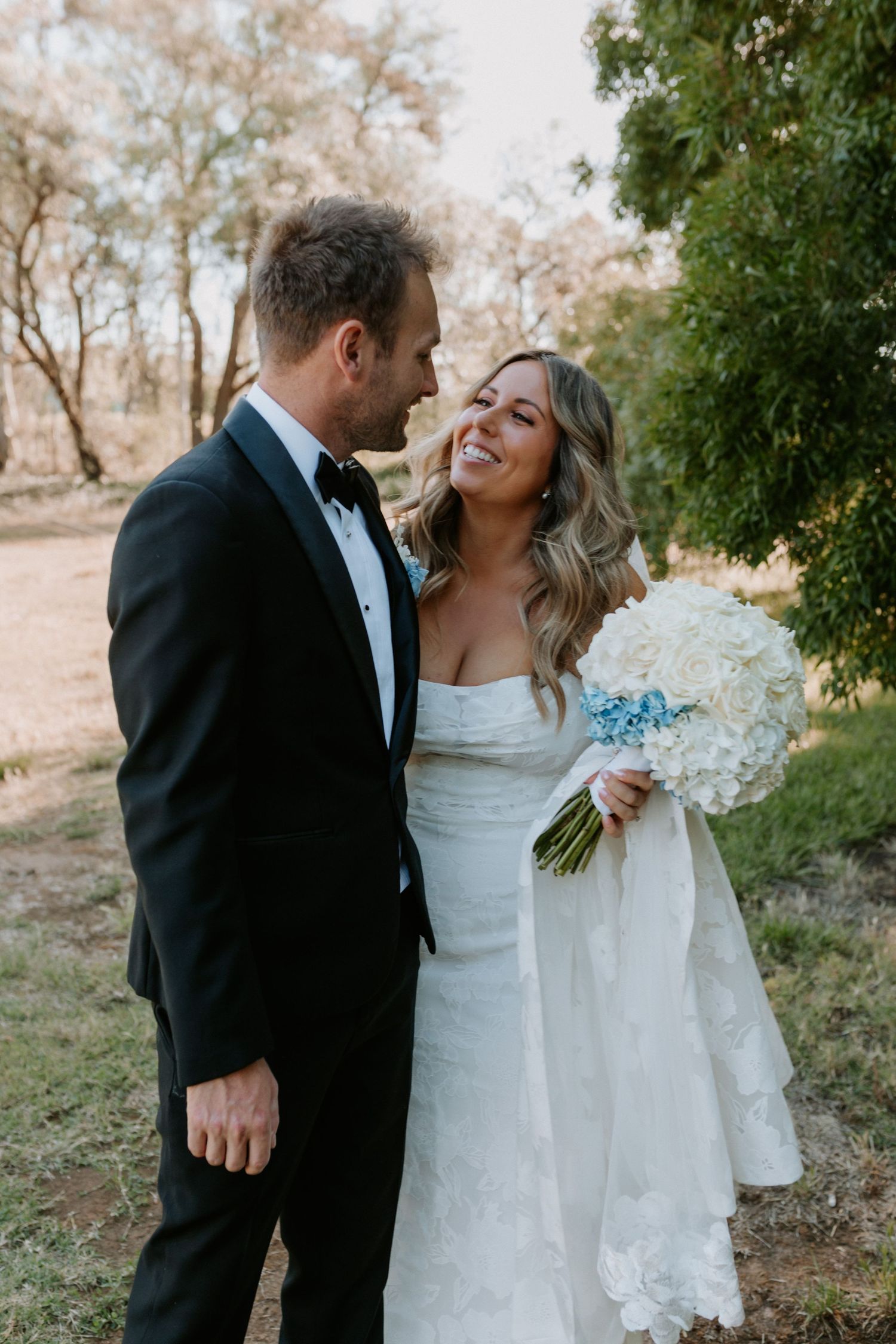 Romantic wedding portrait showing a couple sharing a joyful moment with white hydrangea bouquet in an outdoor setting.