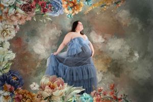 Artistic maternity portrait with flowing blue dress against floral painted backdrop.