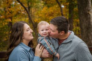A joyful family moment captured outdoors during autumn with fall foliage in the background.