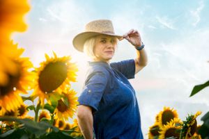 A figure in a cowboy hat stands among bright yellow sunflowers against a blue sky.