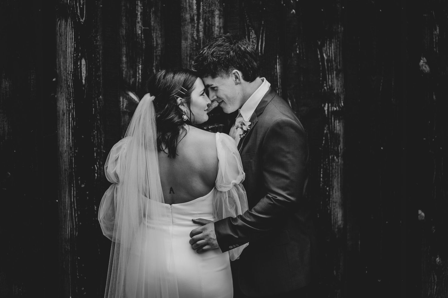 Classic black and white wedding portrait showing tender embrace under rustic wooden backdrop.