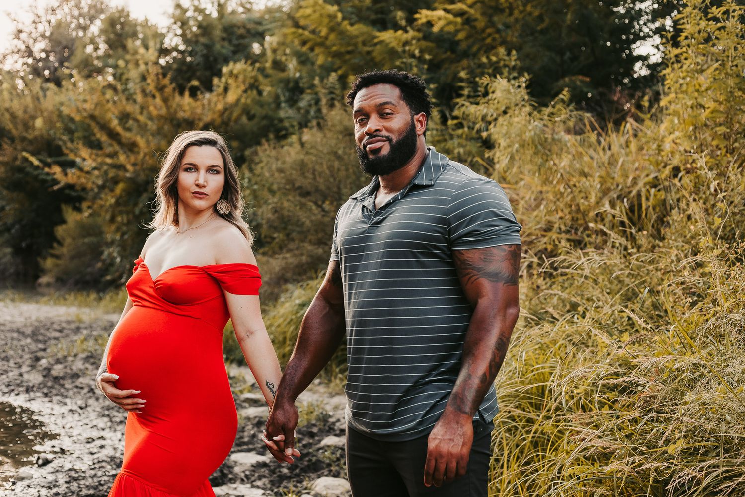 Pregnant woman and husband hold hands at a park at golden hour