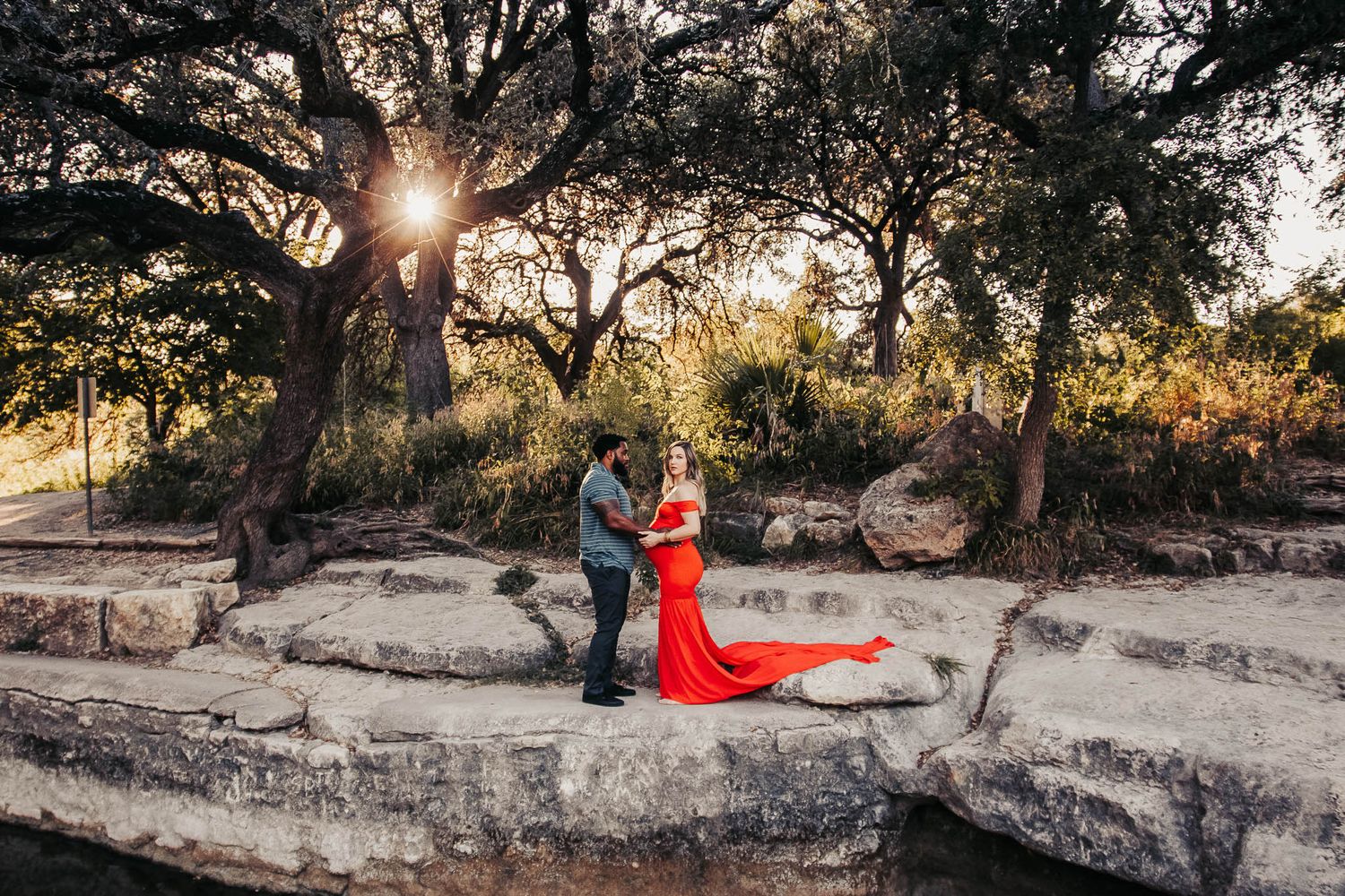 Wide-shot of an expecting mother and father surrounded by trees at golden hour