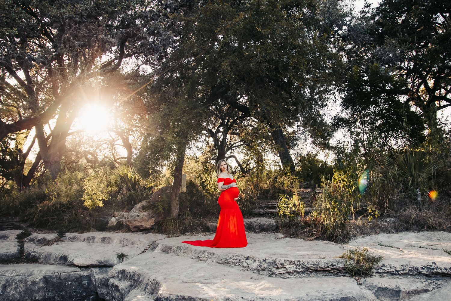 Pregnant woman in dress with a glorious sun shining through trees