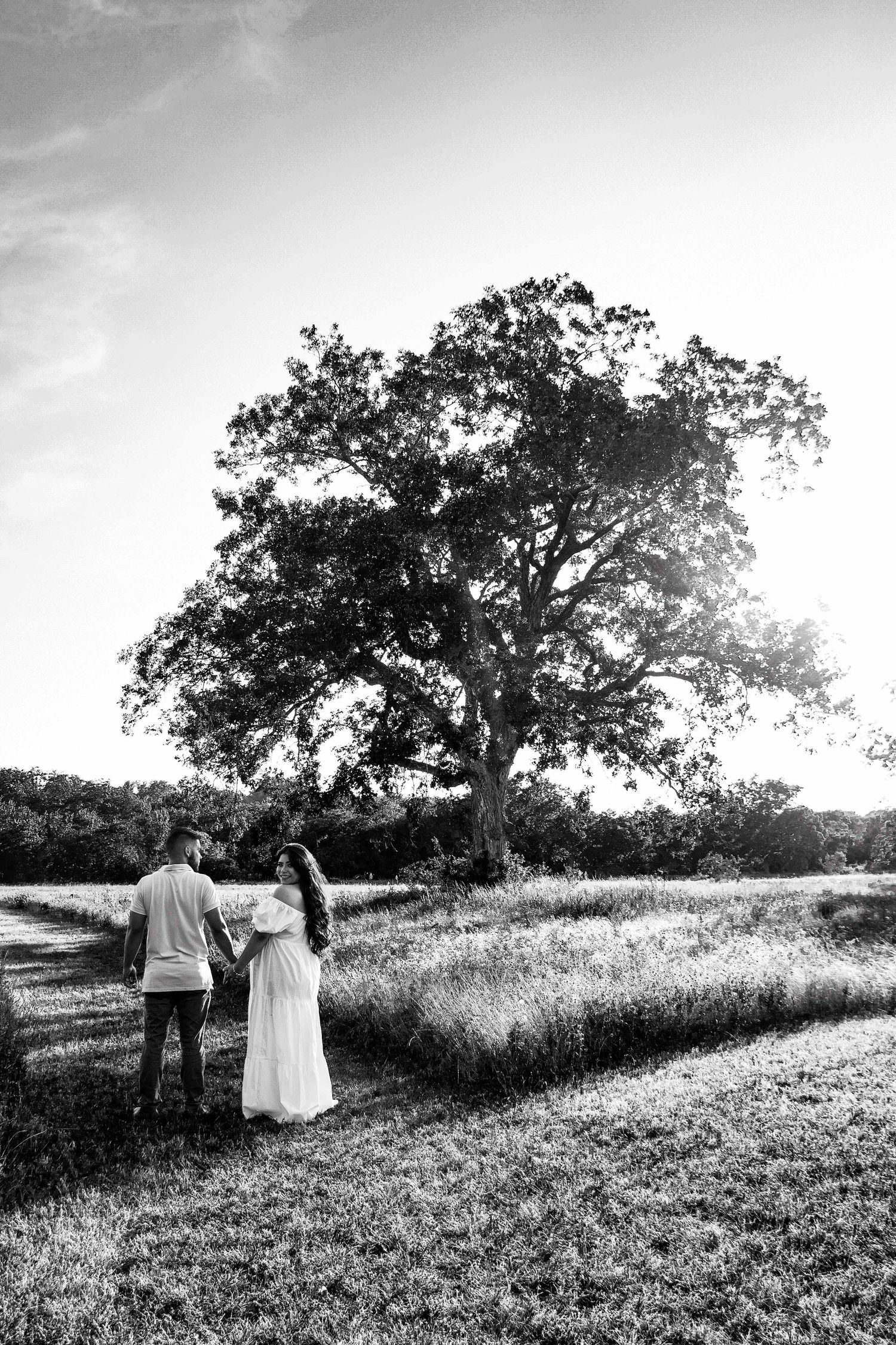 Expecting couple walking into a field with a giant tree about them