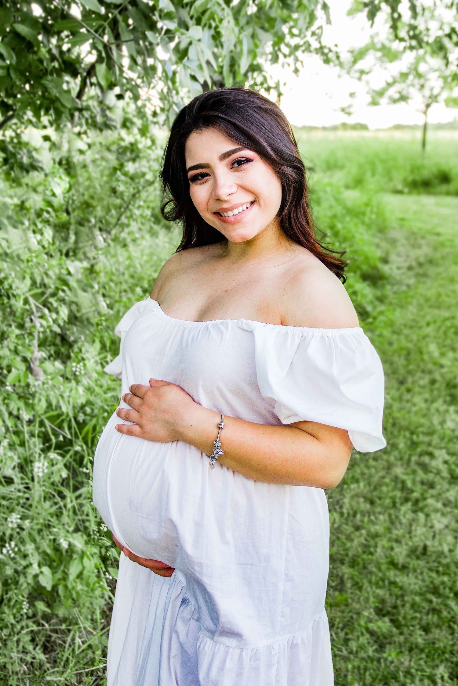 Expecting woman wearing a white dress, holding her pregnant belly