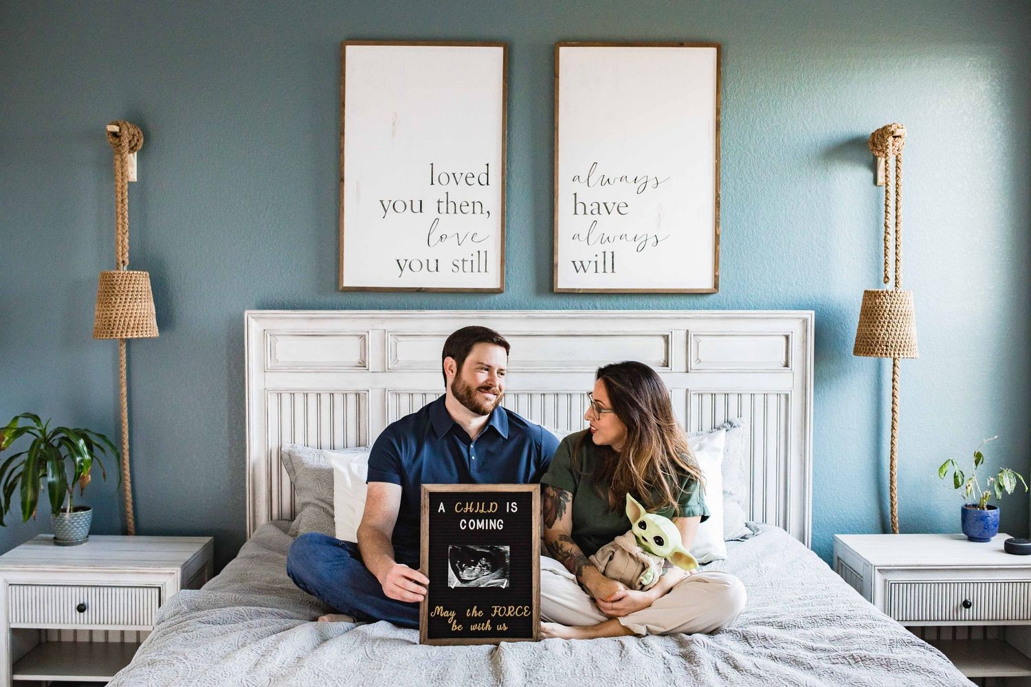 Father-to-be and expecting mother sitting on bed holding up a sign announcing their pregnancy