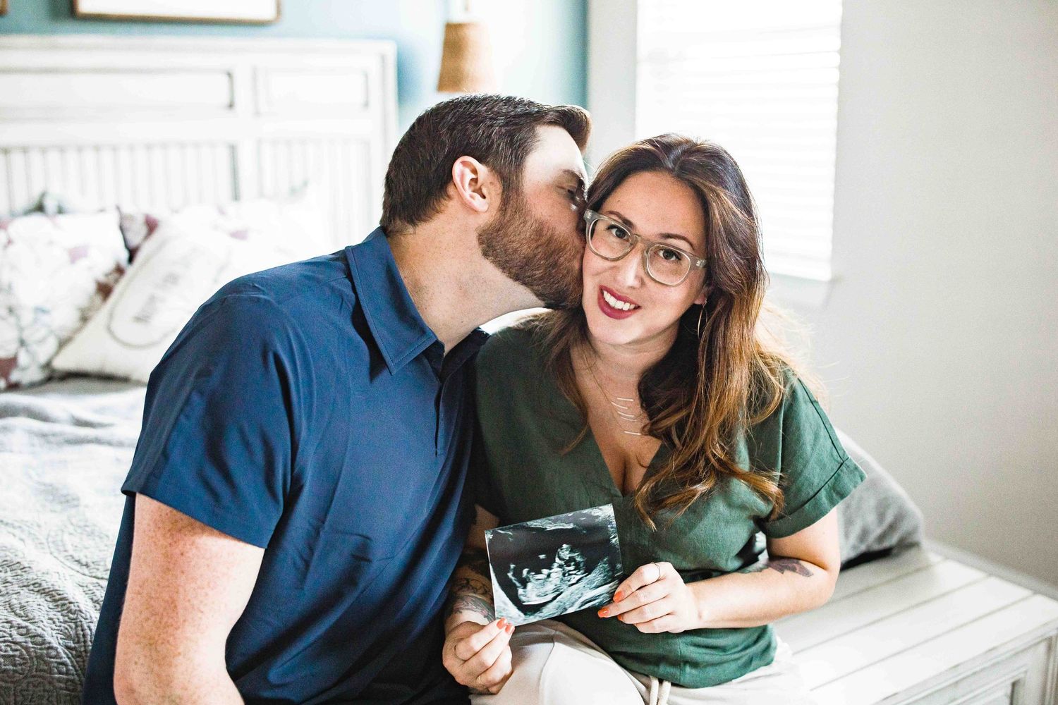 Father-to-be kisses expecting mothers cheek as she holds ultrasound photo up