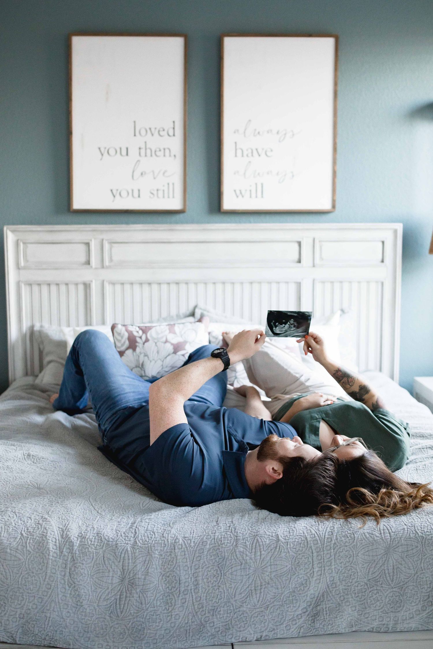 Expecting mother and father laying in bed, holding up baby ultrasound photo