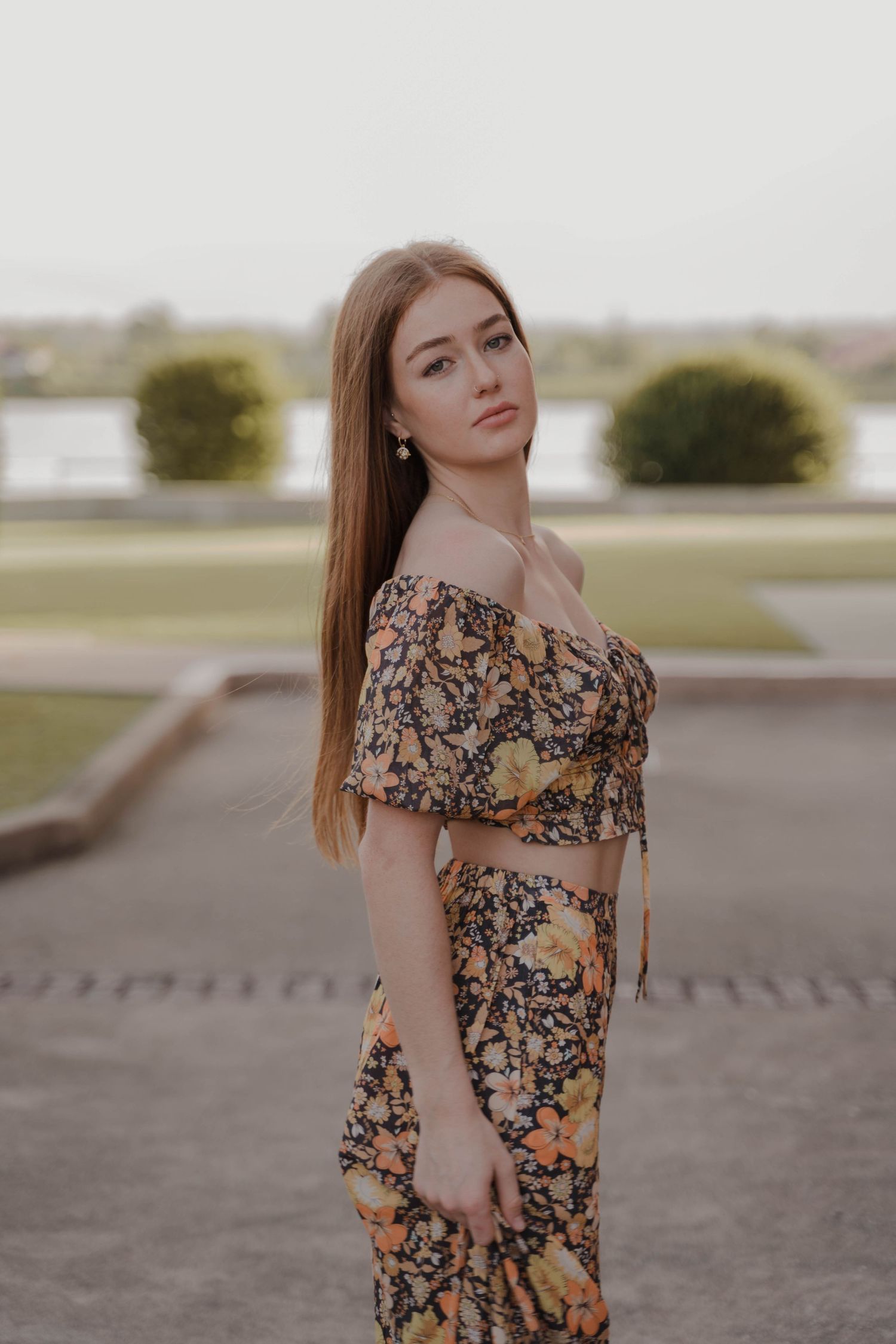 Woman in floral two-piece outfit poses outdoors in soft evening light.
