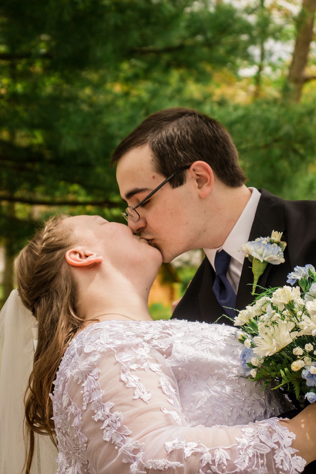 Romantic wedding couple sharing a kiss outdoors with white flowers and lace dress details.
