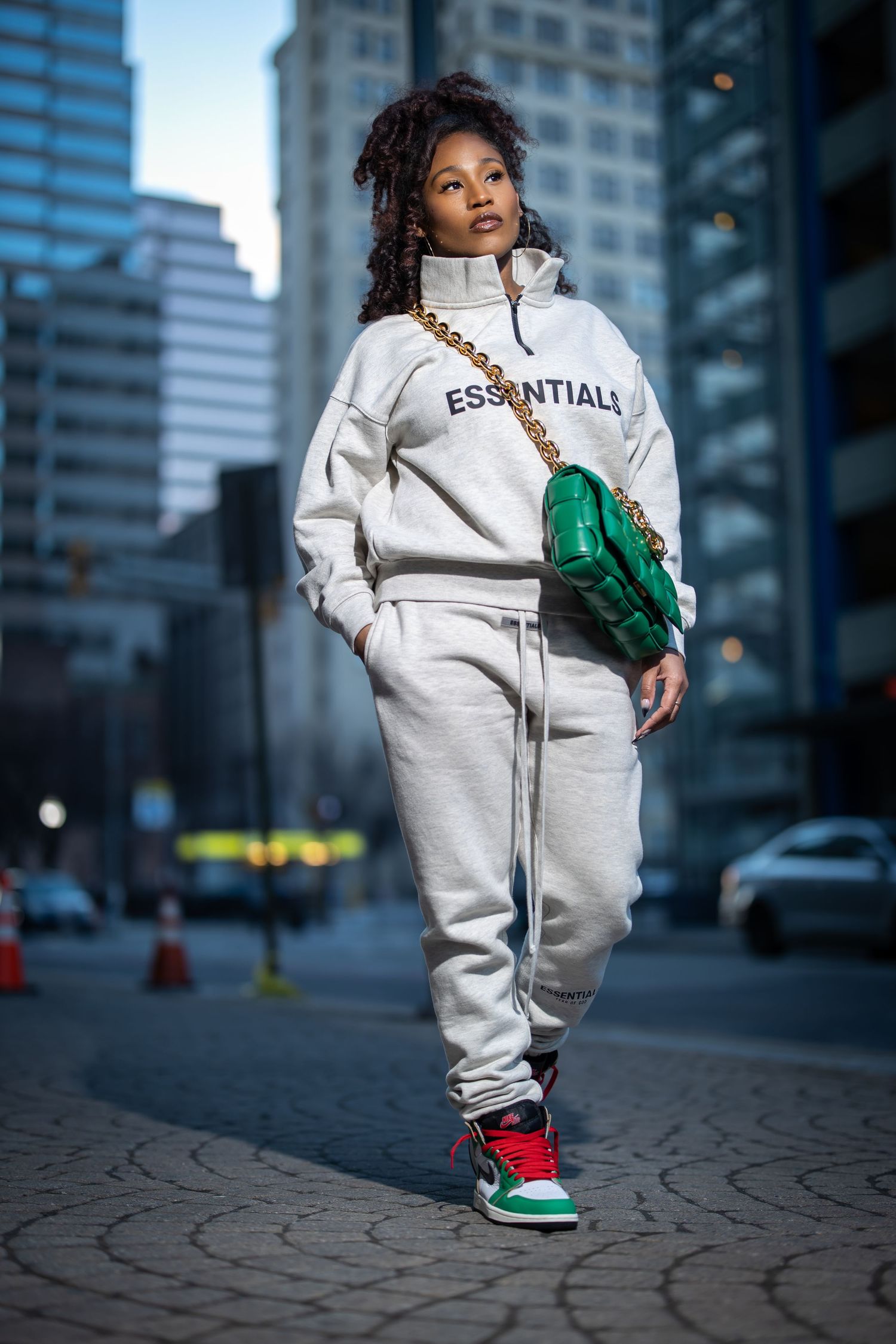Stylish streetwear look featuring cream tracksuit, green bag and red sneakers in city setting.