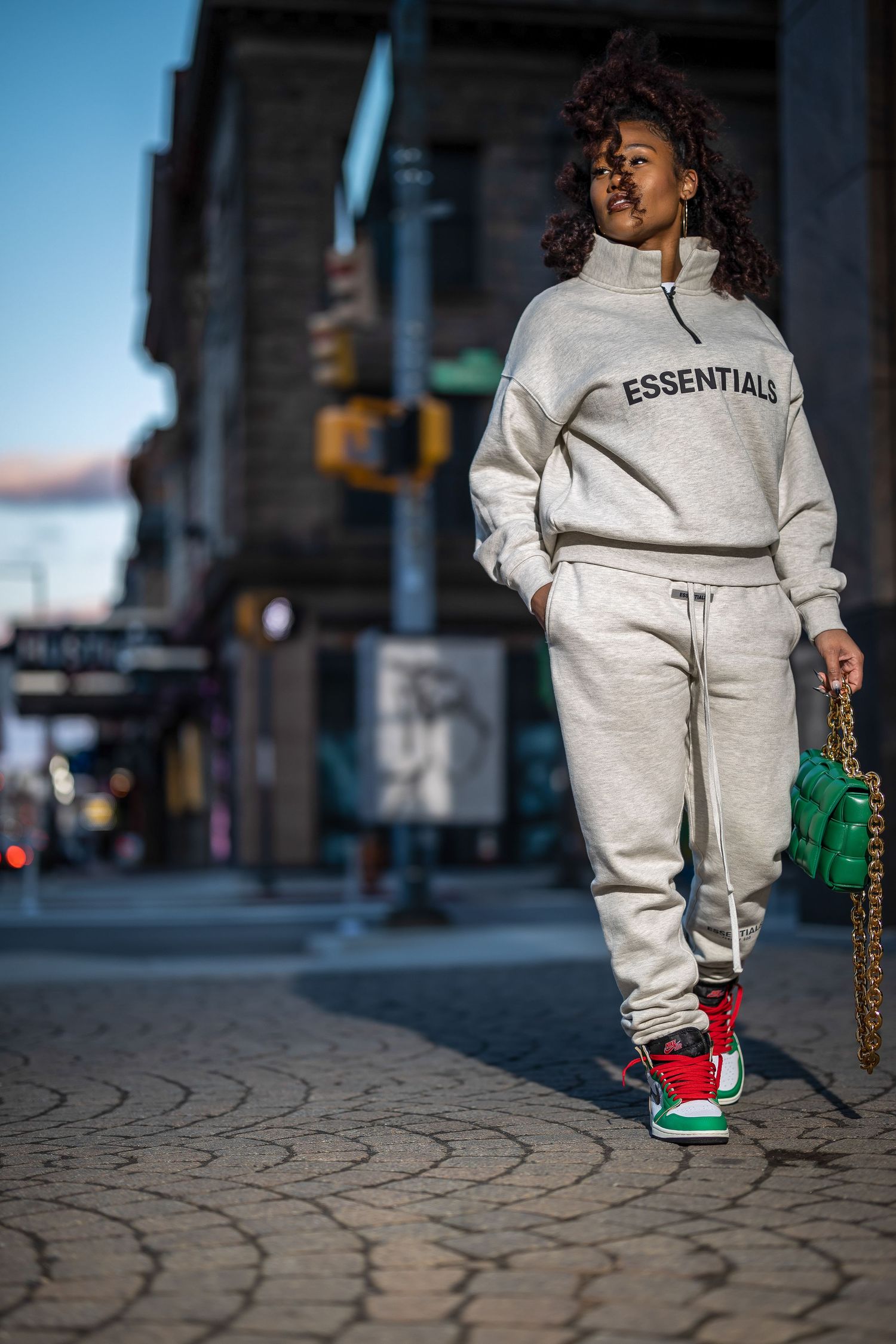 Street style photo showing cream colored tracksuit and green accessories on textured pavement.