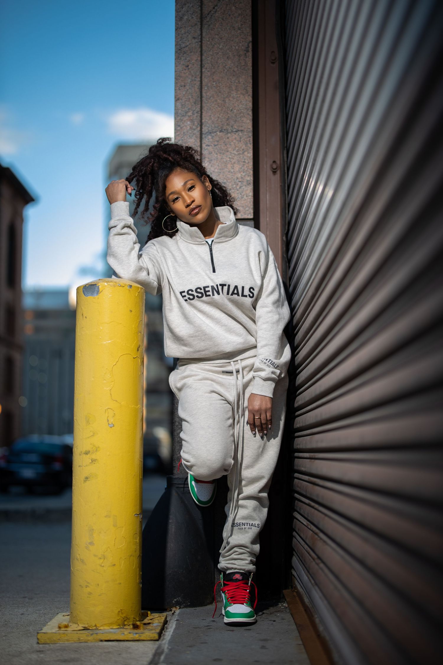 Urban fashion shot showing loungewear outfit against industrial wall with yellow bollard.