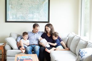 A family gathers on a gray couch reading together underneath a framed map on the wall.