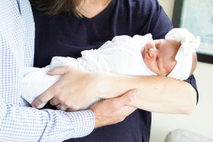 A newborn baby swaddled in white being cradled in loving arms.