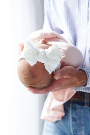 A gentle close-up of a newborn with white bow being cradled.