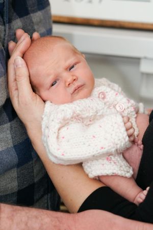 Sleeping newborn wearing a white knitted sweater held in caring hands.