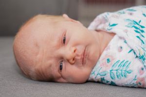 Close-up portrait of a newborn baby in teal patterned swaddle looking at camera.