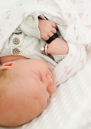 Sleeping baby in white knit cardigan with tiny hand clutching blanket.