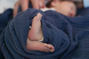 A tiny baby foot peeks out from soft navy blue blanket wrapping.