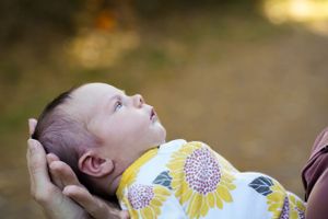 Baby in yellow floral outfit gazing upward during outdoor portrait.