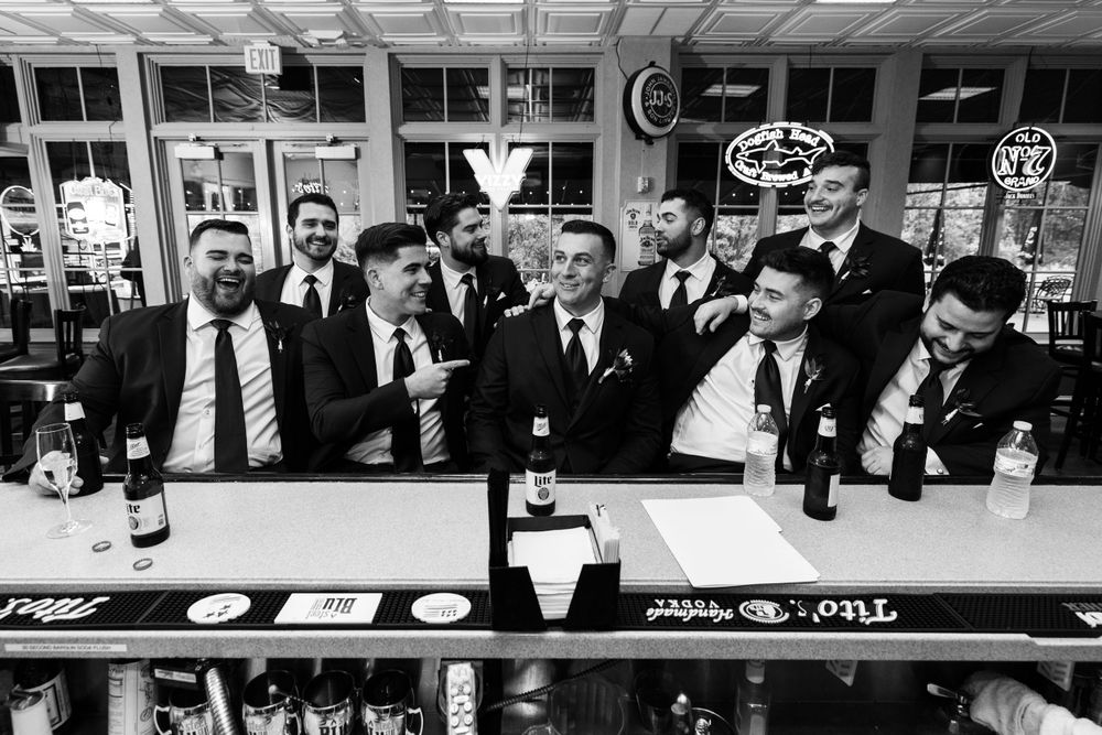Groom and groomsmen laughing together at a bar in black and white wedding photo.