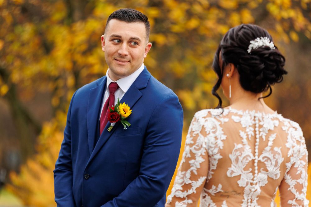 Groom in navy suit smiling at bride during fall outdoor first look wedding moment.