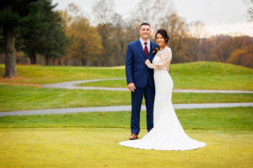 Bride and groom posing together on a lush golf course with fall foliage background.