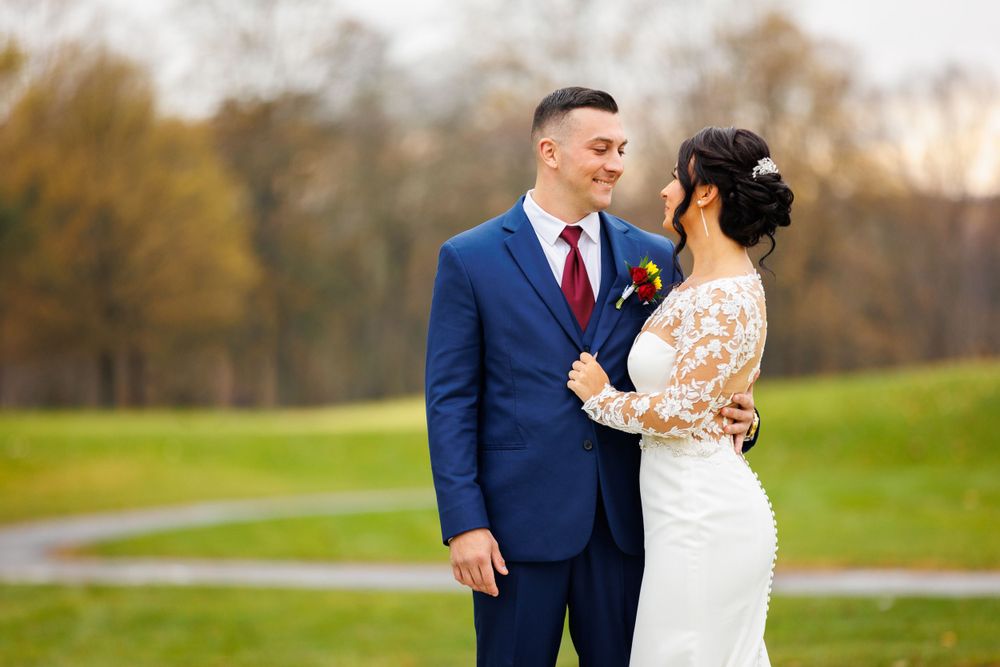 Bride and groom gazing at each other on a golf course surrounded by autumn trees.