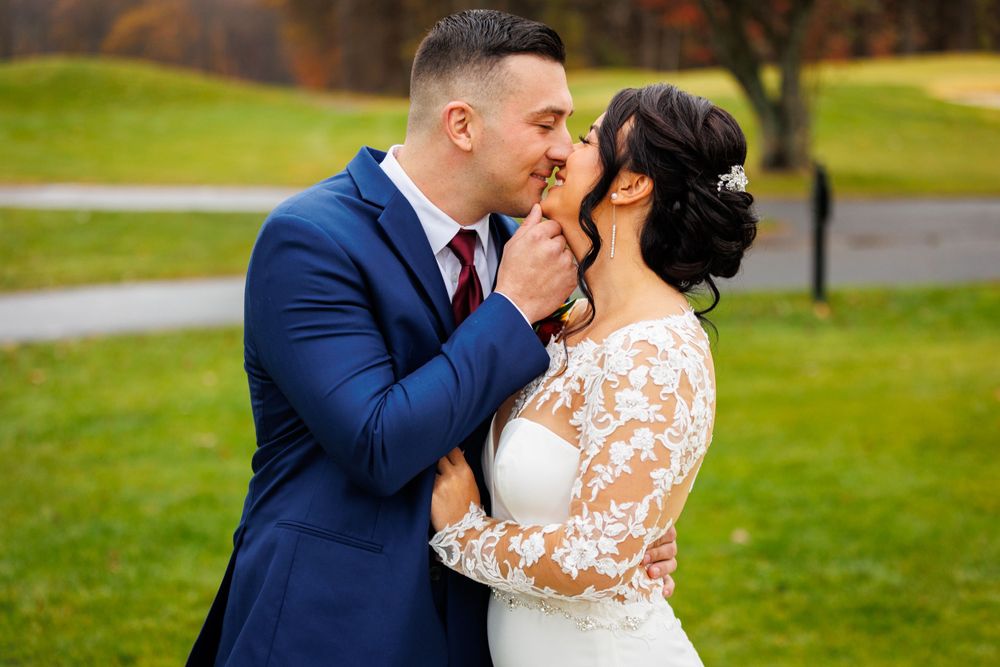 Groom in navy suit kissing bride in lace wedding gown on an autumn golf course.