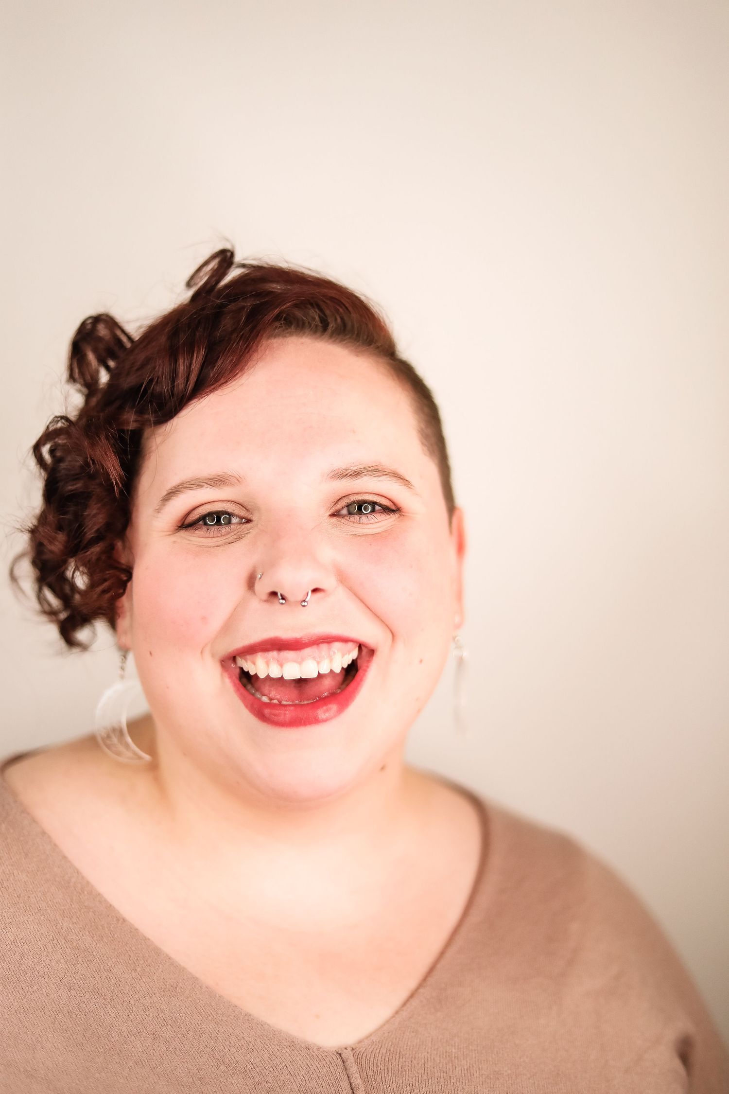 Jenn is smiling, open mouth with teeth at the camera. Her hair is curly and pulled over to one side.