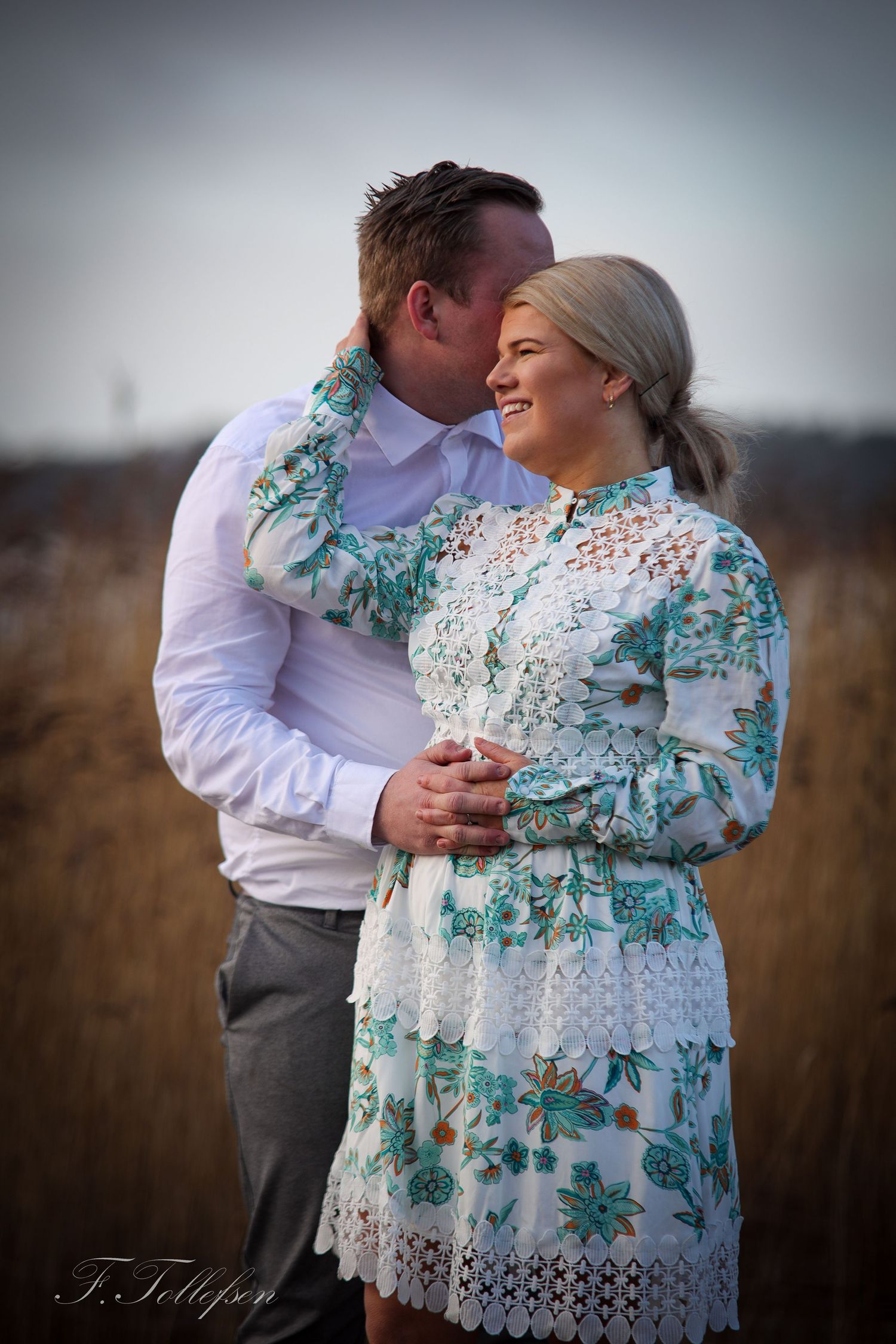 Romantic couple embracing outdoors in a winter field, woman wearing a floral lace dress.