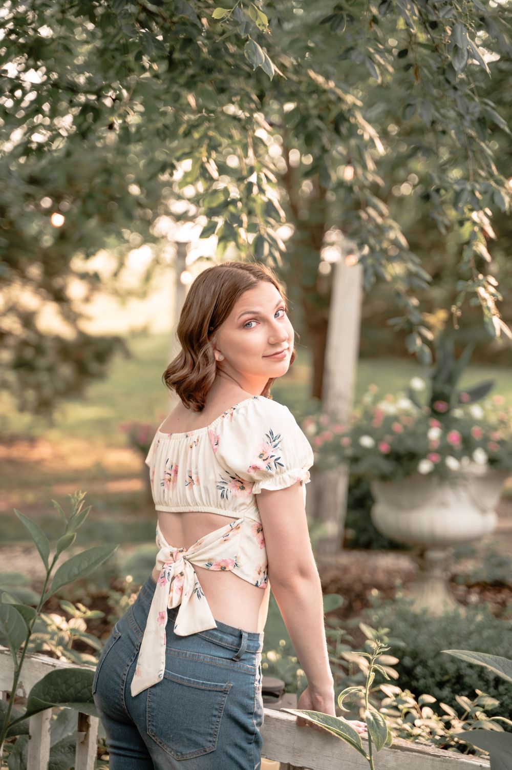 Garden portrait in floral crop top and high-waisted jeans with natural lighting.