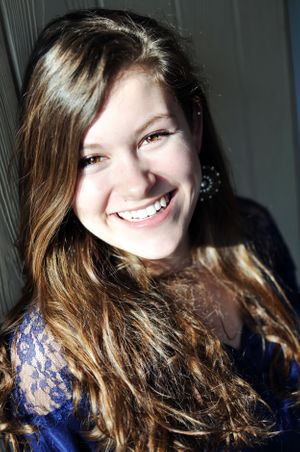 Natural portrait with genuine smile in blue lace top against dark background.