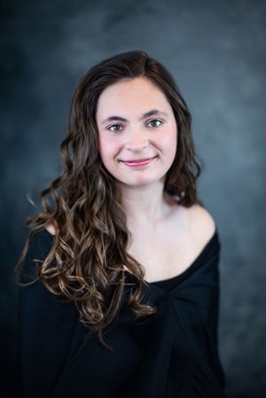 Portrait of woman in black sweater with wavy brown hair against dark background.