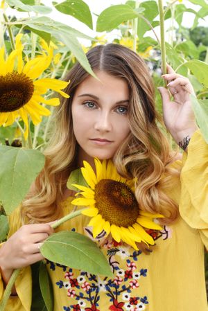 Portrait among sunflowers wearing a yellow embroidered dress against natural garden backdrop.