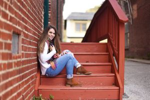 Someone in casual attire sitting on red painted stairs near brick buildings.