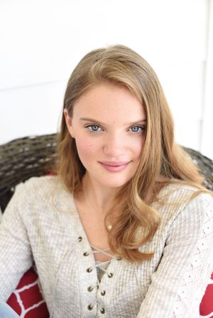 Portrait of a person in a cream colored lace-up sweater sitting in a wicker chair.