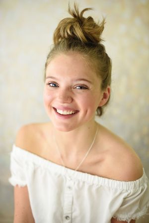 Portrait of a person wearing an off-shoulder white top with a messy bun hairstyle.